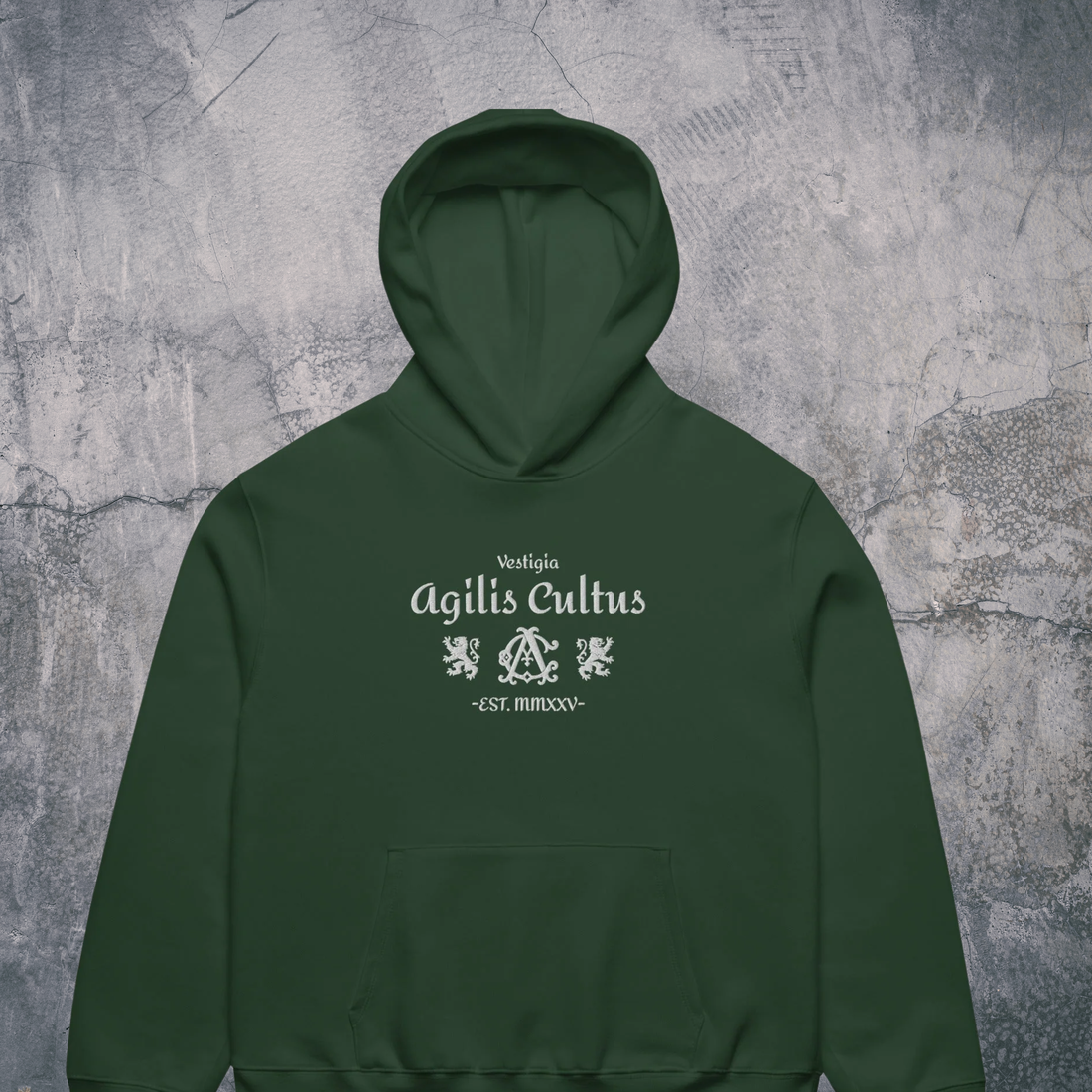 dark green Agilis Cultus hoodie with minimalist crest and typography, centered on neutral textured background, modern heritage streetwear