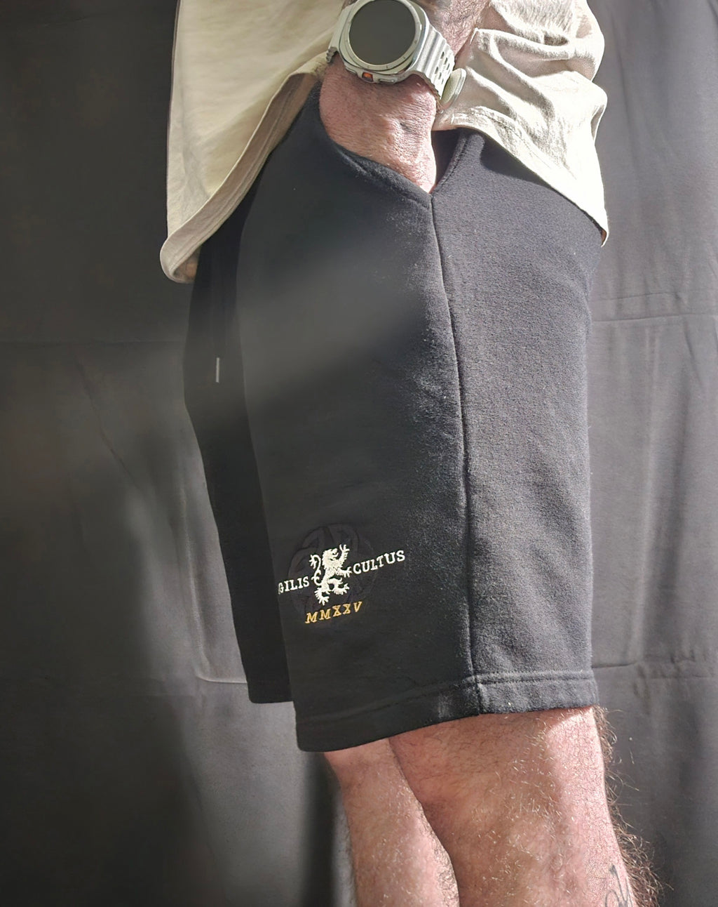 Person wearing black shorts with a logo and text, standing against a dark background