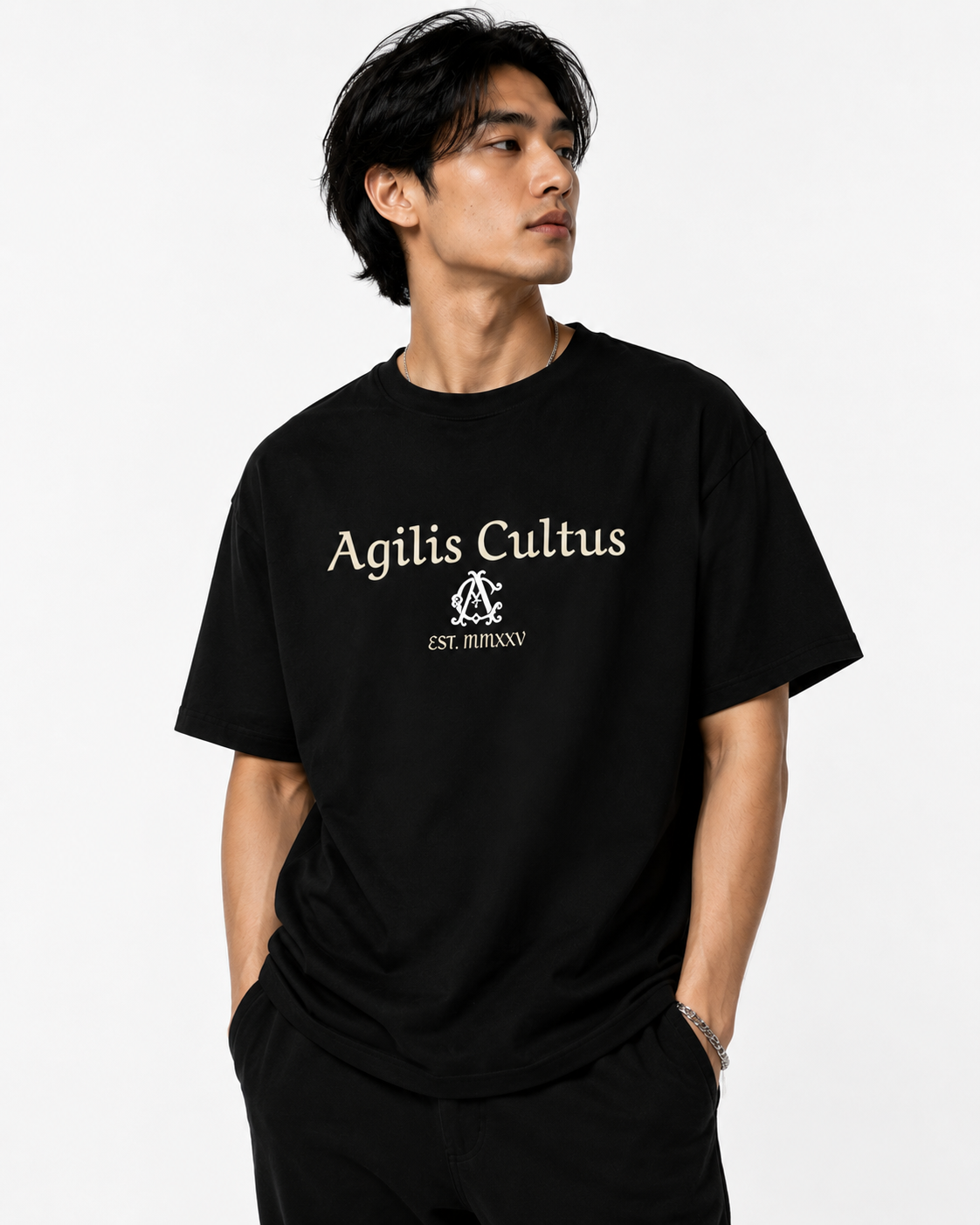 Asian male model wearing a black Agilis Cultus graphic t-shirt with ivory logo text and monogram artwork on a clean white studio background.