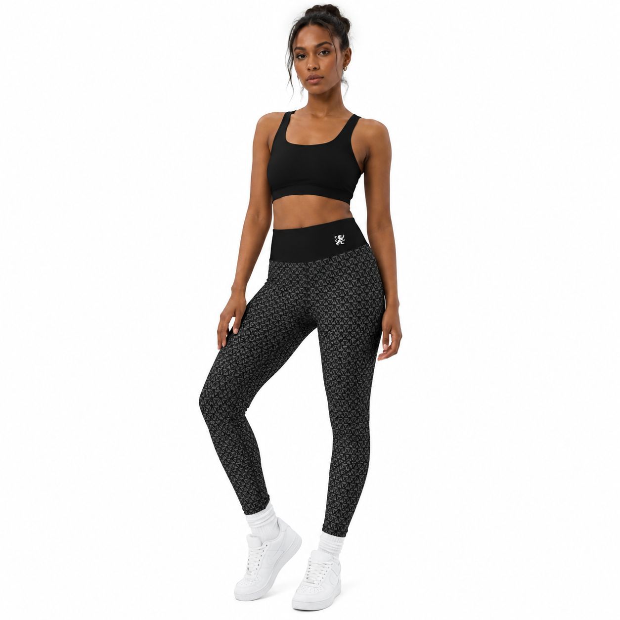 Female model wearing black Agilis Cultus patterned leggings with a high waistband, black sports bra, and white sneakers on a clean white studio background.