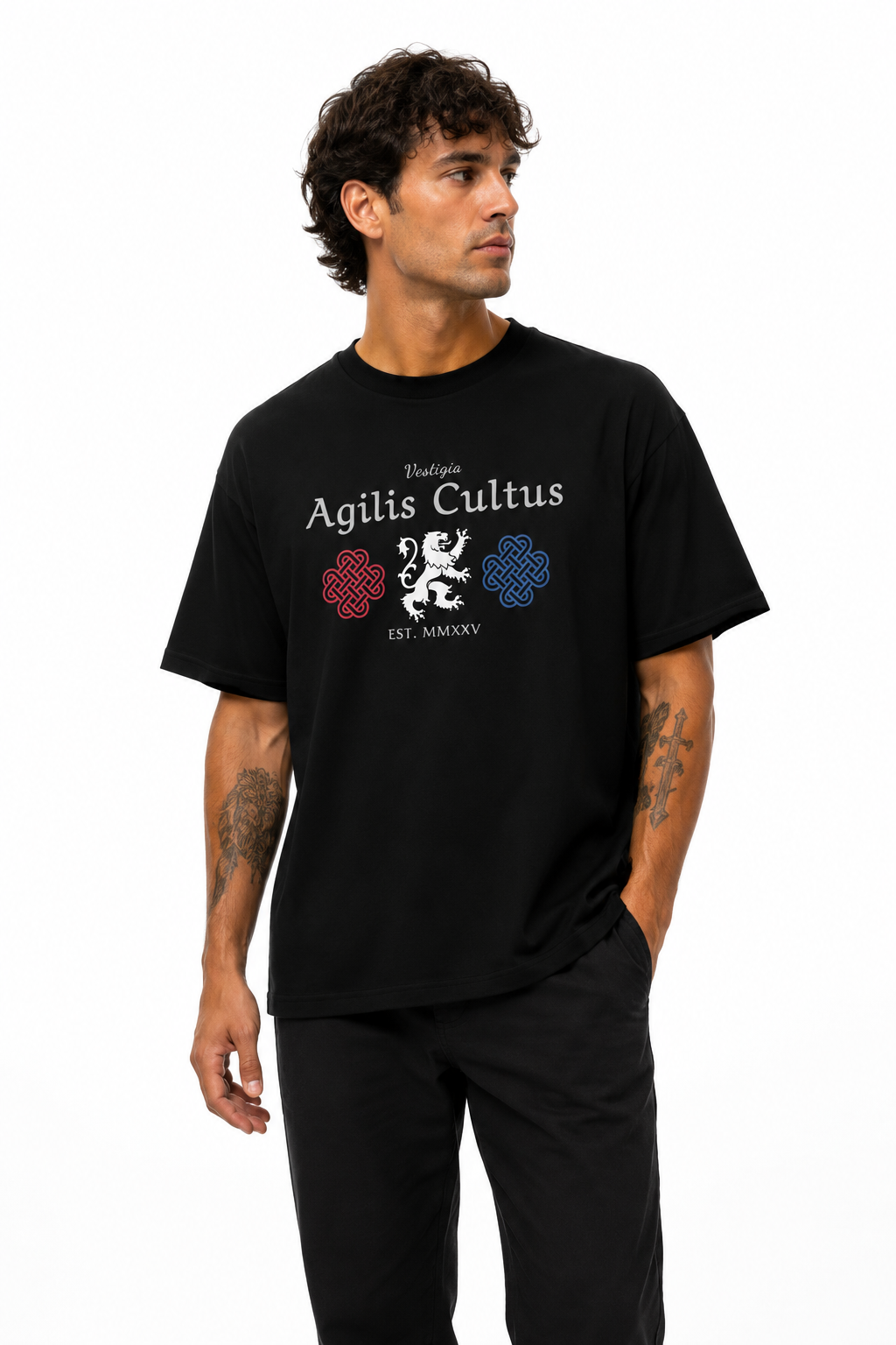 Male model wearing a black Agilis Cultus Vestigia graphic t-shirt with heraldic lion artwork and red and blue knot designs on a clean white studio background.