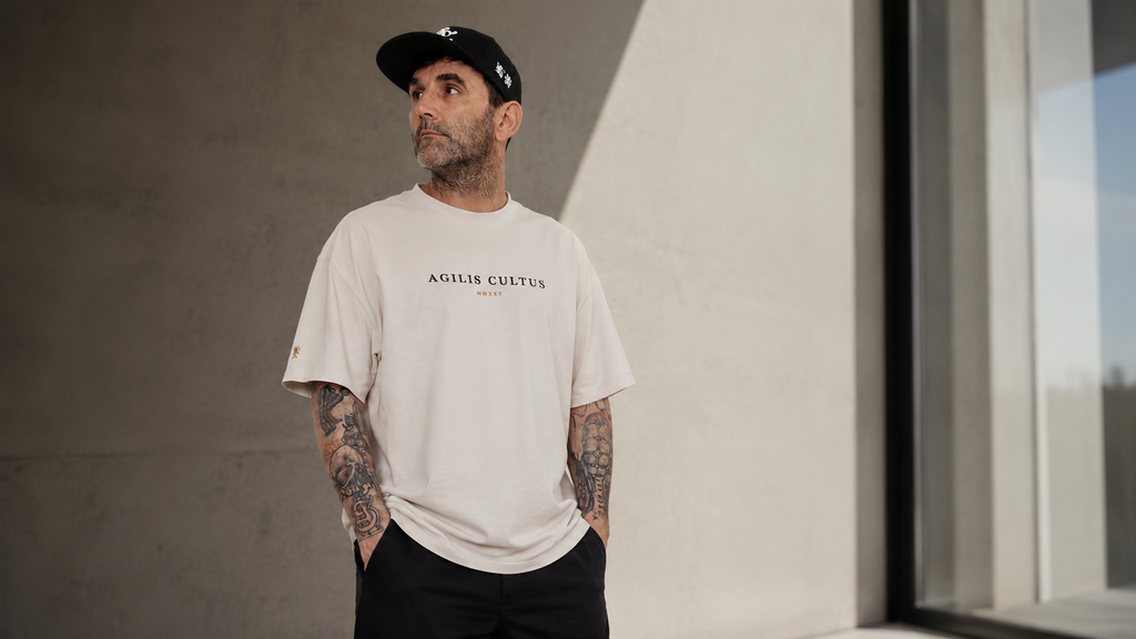 Man wearing a faded bone t-shirt with text, standing against a neutral wall.
